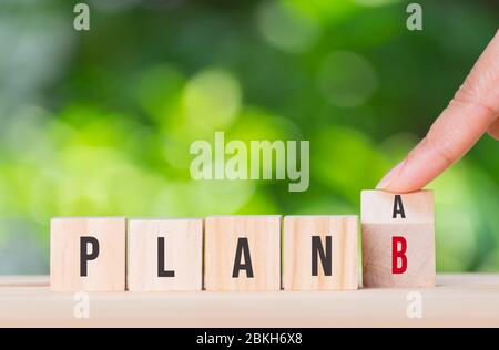 Mano capovolgere cubo di legno con LA parola PIANO A per PIANIFICARE B su sfondo verde bokeh. Concetto di business plan. Crisi di Covid-19. Spazio per la copia per gli inserzionisti. Foto Stock