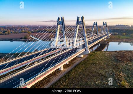 Nuovo moderno ponte doppio con stiva per cavi con ampie strade a tre corsie sul fiume Vistola a Cracovia, Polonia, e la sua riflessione in acqua all'alba. Parte di Foto Stock