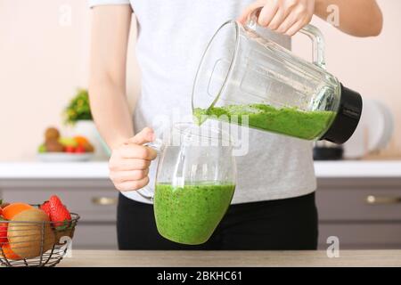 Donna che versa frullato sano nella brocca in cucina Foto Stock