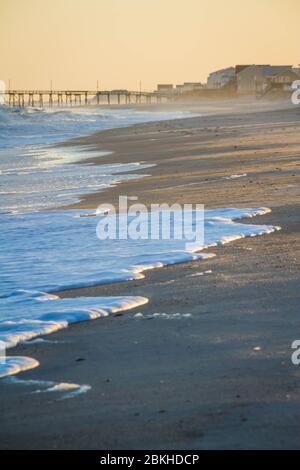 Onde di bianco schiuma di mare lavarsi su una spiaggia alla luce della sera. Foto Stock