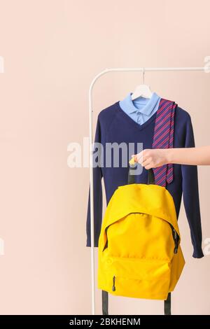 Elegante uniforme scolastica appesa su rack e mano femminile con zaino su sfondo colorato Foto Stock