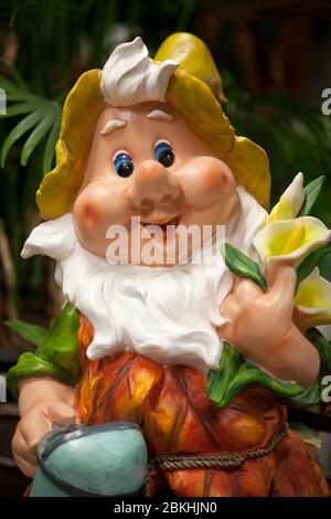 Nana carina che vive in un giardino. Decorazione sorridente gnome giardino su uno sfondo sfocato. Elfo divertente in giardino. Figurina nana felice. Foto Stock