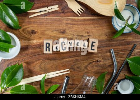 Il mattone di legno con le parole 'RICICLARE' su sfondo di legno. CONCETTO ECO con simbolo di riciclaggio e foglie. Foto Stock