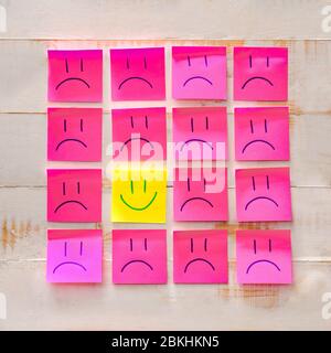 Un foglio di carta con faccia felice disegnata fra i fogli con quei tristi. Concetto di differenza e unicità Foto Stock