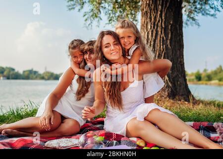 Giorno della madre. Famiglia che ha pic-nic in primavera fiume al tramonto. Madre, nonna e bambini che si abbronzano ridendo. Foto Stock