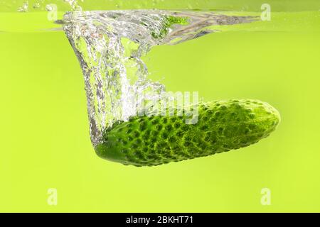 Caduta di cetrioli freschi in acqua contro sfondo colore Foto Stock