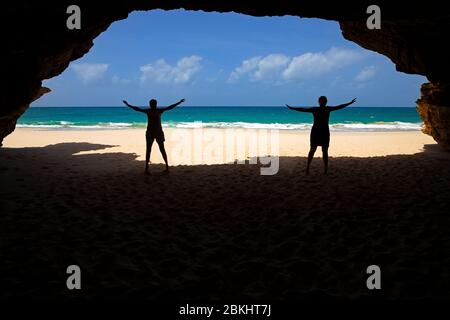 Due turisti sagomatati all'ingresso della grotta di mare a Praia de Santa Mónica, spiaggia sabbiosa sull'isola di Boa Vista, Capo Verde / Cabo Verde Foto Stock