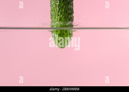 Caduta di cetrioli freschi in acqua contro sfondo colore Foto Stock