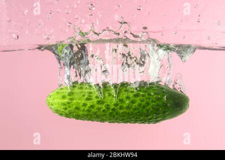 Caduta di cetrioli freschi in acqua contro sfondo colore Foto Stock