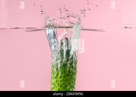 Caduta di cetrioli freschi in acqua contro sfondo colore Foto Stock