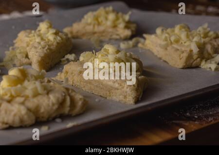 Scones di formaggio crudo seduti su forno pergamena su un vassoio da forno gli scones sono stati coperti con formaggio grattugiato Foto Stock