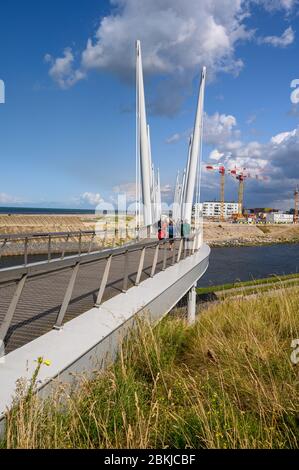 DUNKERQUE, FRANCIA - 13 AGOSTO 2019: Persone che attraversano la Passerelle du Grand Large - Ponte grande - a Dunkerque in una giornata di sole con la città in rovina Foto Stock