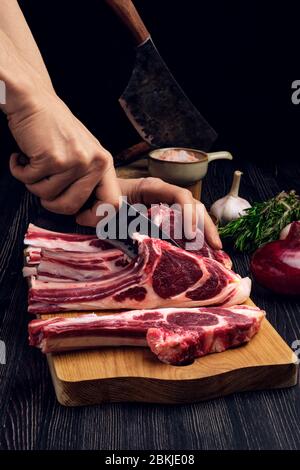 Uomo che taglia rack di agnello su legno asse. Preparazione di carne fresca per la cottura. Foto Stock