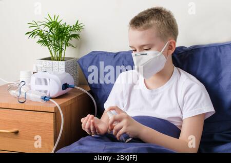 Ragazzo malato in maschera medica protettiva utilizzando igienizzante per le mani. Il bambino siede sul letto. Concetto di focolaio di coronavirus Foto Stock