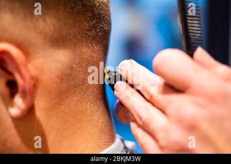 Barber rifinì i capelli di un giovane con un rasoio nel suo barbiere. Primo piano e dettagliato Foto Stock