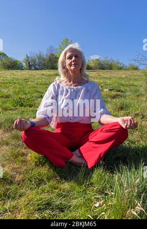 Europa, Lussemburgo, Insenborn, attraente donna anziana meditata vicino Lac Sûre Foto Stock