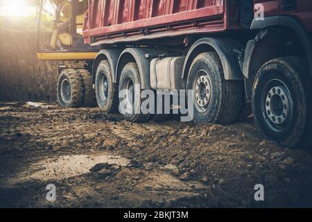 Uomo in escavatore che sposta la sporcizia sul dumper in cantiere. Foto Stock