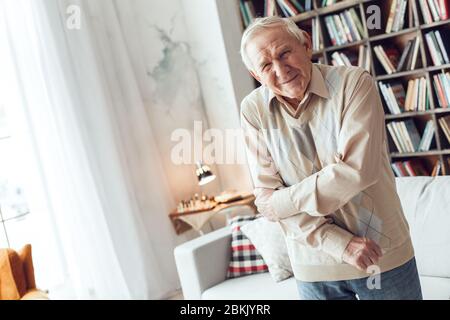 Uomo anziano da solo in piedi alla biblioteca avendo dolore nel braccio Foto Stock