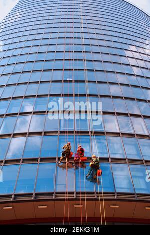 Tre lavoratori uomini in abiti da lavoro rossi e scuri che puliscono l'esterno Foto Stock