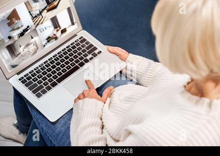 Pensionamento. Donna anziana seduta a casa facendo shopping online sullo schermo del notebook vista posteriore ravvicinata Foto Stock