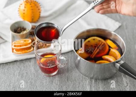 mano con mestolo versando il vin brulé caldo al bicchiere Foto Stock