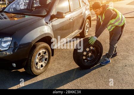 Il conducente deve sostituire la vecchia ruota con una ruota di scorta. Uomo che cambia ruota dopo un guasto auto. Trasporto, concetto di viaggio Foto Stock