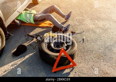 Un conducente o un lavoratore ripara un'auto rotta sul lato della strada. Vista dall'alto. L'uomo è sotto la macchina Foto Stock