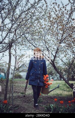 ragazza con lattina d'acqua, tulipani e attrezzi in giardino. primavera e giardinaggio Foto Stock