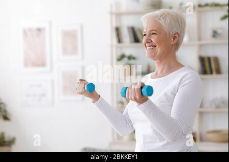 Palestra a casa. Formazione di donne anziane con i manubri nel soggiorno Foto Stock