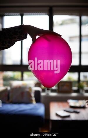 La mano di una donna tiene un palloncino rosa a casa. Foto Stock