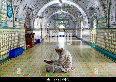 Un Imam è visto seduto all'interno della moschea mentre legge il santo Corano durante il mese santo di Ramadan. Ramadan è il mese olistico del calendario islamico in cui i devoti stanno digiunando dall'alba al tramonto. I musulmani di tutto il mondo celebrano il mese del Ramadan e hanno trovato vari modi per celebrare questo mese del Ramadan, poiché le restrizioni poste dai paesi per frenare la diffusione del Coronavirus hanno chiuso le moschee per impedire gli incontri. Foto Stock