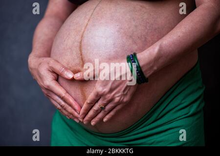 Stomaco di una donna incinta nel terzo trimestre con le mani sul feto sotto forma di cuore Foto Stock