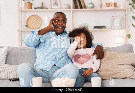 Intrattenimento per la famiglia Lockdown. Scioccato afro americano uomo e spaventata nipote guardare film spaventoso a casa Foto Stock