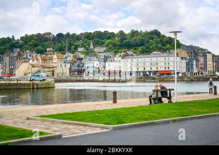 Una coppia in pensione più anziana siede su una panchina del parco e gode della vista del villaggio di pescatori di Honfleur Francia, in Normandia in un pomeriggio parzialmente nuvoloso Foto Stock