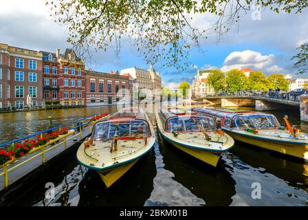 Colorato di giallo e rosso barche tour di attendere in linea per passeggeri per turismo su un importante canale di Amsterdam, Paesi Bassi Foto Stock