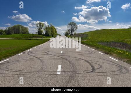 Segni di gomma dalle ruote su una superficie stradale tra campi verdi rigogliosi in una giornata di sole Foto Stock