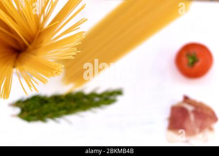 Ingredienti di cottura su sfondo rustico di legno bianco. Pasta, spaghetti crudi, pomodoro, rosmarino, prosciutto/cucina tipica italiana Foto Stock