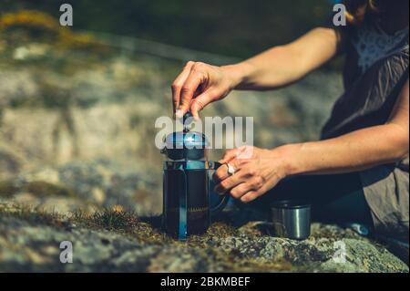 Una giovane donna utilizza una pressa francese per fare il caffè all'aperto in natura Foto Stock