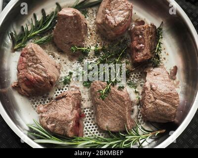 Filetto di manzo biologico con rosmarino fresco e timo in una padella di acciaio inossidabile, vista dall'alto, cucina con erbe fresche, cibo biologico o cibo sano Foto Stock