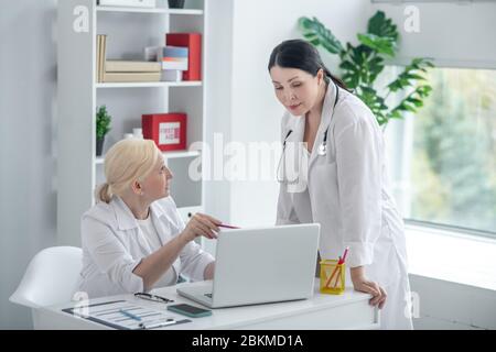 Due medici donne in abiti bianchi che hanno una discussione sul caso Foto Stock