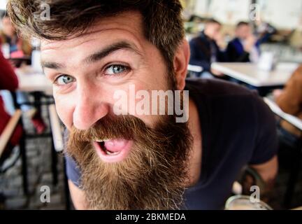 Ragazzo che riposa sulla terrazza del caffè, primo piano. Hipster, cliente, visitatore su Happy Face siede al cafe all'aperto. Concetto di macho barbuto. Uomo con barba e baffi di buon umore mentre si rilassa nella terrazza del bar Foto Stock