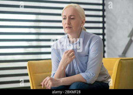Donna adulta triste seduta su una sedia vicino alla finestra. Foto Stock