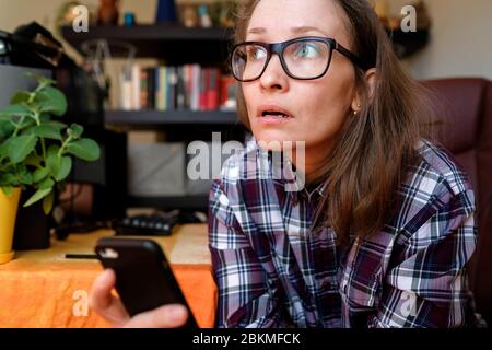 La giovane donna è sorpresa. Tenere il telefono in mano e ascoltare. Abiti da casa, lavoro a casa. Foto Stock