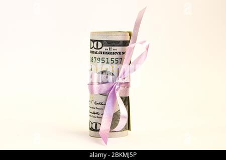 Piccolo dono del dollaro, pacchetto di fatture di cento dollari legati con un nastro rosa. Dollari isolati su sfondo bianco Foto Stock