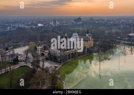 Budapest, Ungheria - veduta aerea del Castello di Vajdahunyad nel Parco della Città (Varosliget) con il Lago del Parco della Città e una bella alba dorata dietro Foto Stock