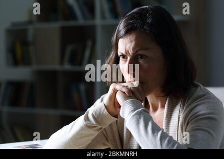 Donna arrabbiata di mezza età che pensa guardando via seduto da solo di notte nel soggiorno a casa Foto Stock