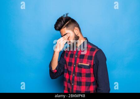 Giovane indiano che indossa camicia elegante e cravatta in piedi su isolato sfondo blu con mano sulla testa per il dolore in testa perché stress. Foto Stock