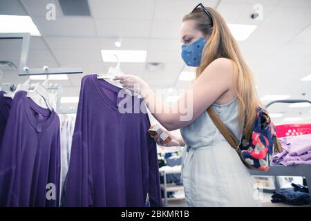 Una donna che indossa una maschera facciale mentre fa shopping in un grande magazzino di abbigliamento. Persone che indossano maschere di stoffa per proteggersi da covid-19 pandemic. Foto Stock