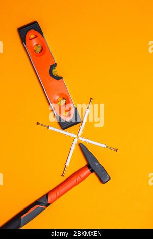 Attrezzi per la riparazione. Martello per chiodi, livella, tassello a parete su fondo arancione. Toolkit per la procedura guidata Foto Stock