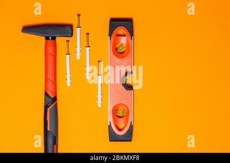 Attrezzi per la riparazione. Martello per chiodi, livella, tassello a parete su fondo arancione. Toolkit per la procedura guidata Foto Stock
